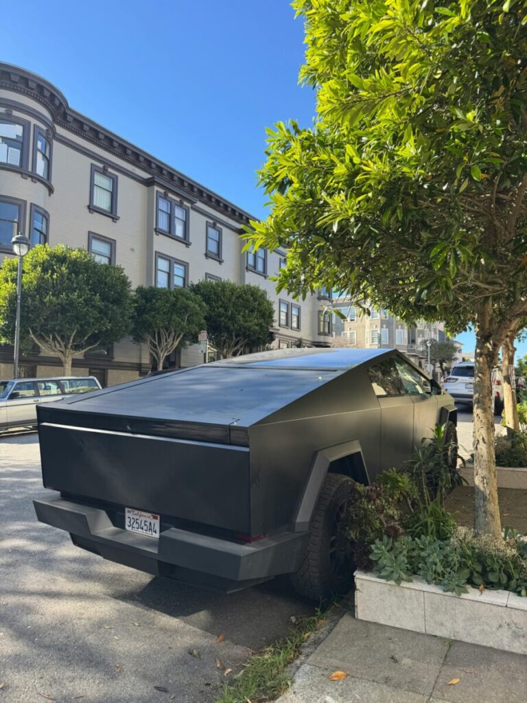 A futuristic vehicle parked under trees on a sunny street in San Francisco, California.